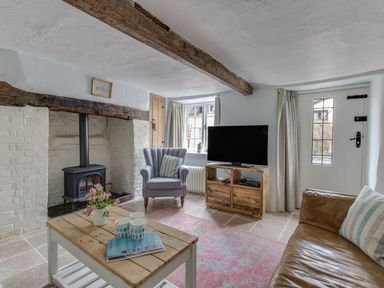 A living room with a wood stove fireplace a wooden coffee table a gray armchair and a leather sofa at Amy Cottage in West Lulworth