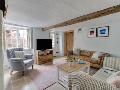 A living room with a brown leather sofa a blue armchair a striped sofa a wooden coffee table a television on a wooden stand and exposed wooden beams at Amy Cottage in West Lulworth
