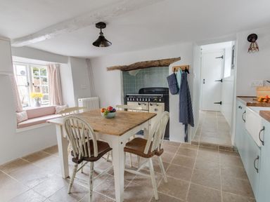 A kitchen with wooden table and chairs fruit bowl stove and window seat at Amy Cottage in West Lulworth