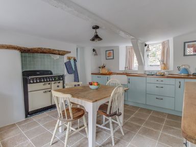 A kitchen with a wooden table and chairs a stove and blue cabinets at Amy Cottage in West Lulworth
