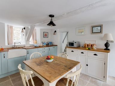 A kitchen with a wooden table and chairs a countertop with a sink cabinets and a microwave at Amy Cottage in West Lulworth