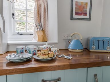 A kitchen countertop with plates forks cups a teapot scones a knife block a kettle and a toaster at Amy Cottage in West Lulworth