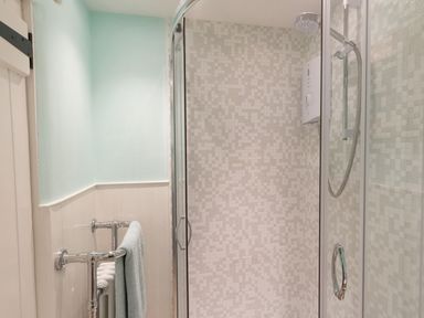 A bathroom with a glass shower enclosure a tiled shower area and a towel rail with a towel at Amy Cottage in West Lulworth