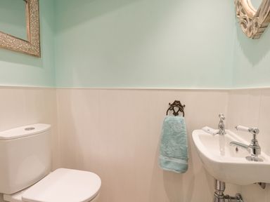 A bathroom with a toilet a sink a towel hanging on a holder and two mirrors at Amy Cottage in West Lulworth