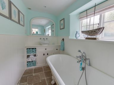 A bathroom with a freestanding bathtub shelves with towels a sink and a mirror at Amy Cottage in West Lulworth