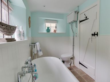 A bathroom with a bathtub toilet and decorative bottles by windows at Amy Cottage in West Lulworth