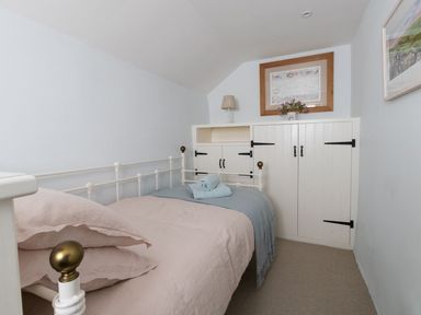 A small bedroom with a single metal bed and built in white cupboards at Amy Cottage in West Lulworth