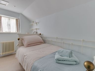 A bedroom with a single bed with blankets pillows and folded towels by a window and radiator at Amy Cottage in West Lulworth