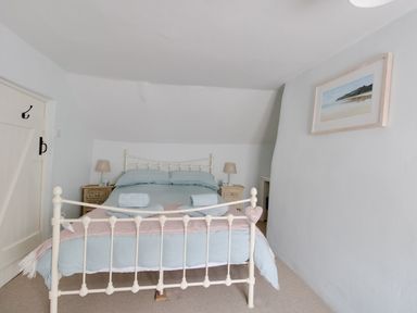 A bedroom with a bed with blue bedding two bedside tables with lamps and a landscape picture on the wall at Amy Cottage in West Lulworth