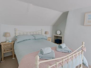 A bedroom with a bed a pink throw towels on the bed bedside tables lamps and a small dressing table with a stool at Amy Cottage in West Lulworth