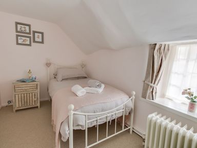 A bedroom with a single bed beside a side table and a window with curtains at Amy Cottage in West Lulworth