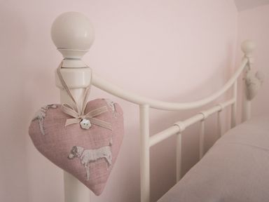 A white metal bed frame with a pink heart-shaped fabric decoration hanging on a bedpost at Amy Cottage in West Lulworth