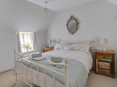 A bedroom with a double bed between two wooden bedside tables with lamps and a window with flowers at Amy Cottage in West Lulworth