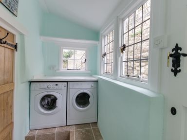 A laundry room with a washing machine and dryer under a countertop near windows and a wooden door at Amy Cottage in West Lulworth