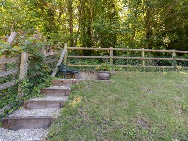 A garden area with wooden steps leading to a bench and a flower pot near a wooden fence surrounded by trees at Amy Cottage in West Lulworth