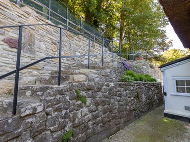 A stone terraced retaining wall with metal railings and plants next to a white building at Amy Cottage in West Lulworth