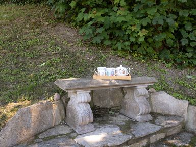 A stone bench with a wooden tray holding a teapot and cups in a garden at Amy Cottage in West Lulworth