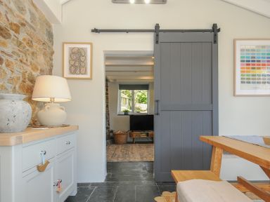 A dining area with a wooden bench table and a gray sliding barn door leading to a living room at Rose Cottage in Callington