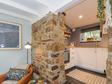 A kitchen with white cabinets and a stone wall next to a leather chair with a pillow at Rose Cottage in Callington
