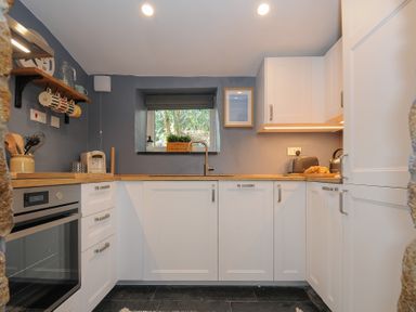 A kitchen with white cabinets wooden countertops a window above the sink and appliances at Rose Cottage in Callington