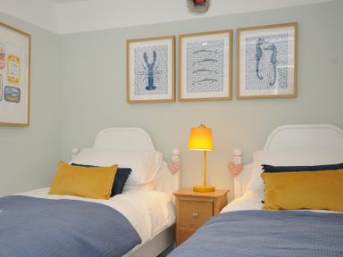 A bedroom with two single beds a wooden nightstand with a yellow lamp and framed pictures of sea creatures on the wall at Rose Cottage in Callington