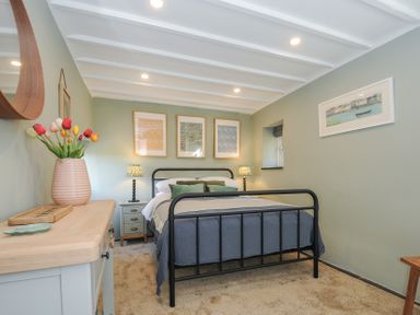 A bedroom with a black metal bed frame a wooden dresser with flowers and three framed pictures above the bed at Rose Cottage in Callington