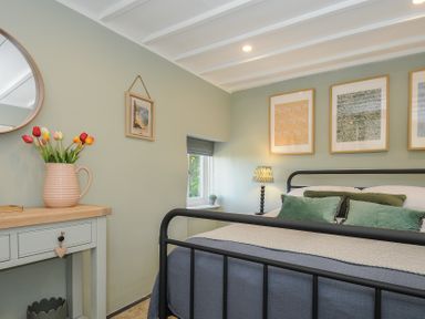 A bedroom with a metal framed bed green cushions and framed pictures above the bed at Rose Cottage in Callington
