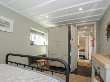 A bedroom with a black metal bed frame a gray wardrobe a wooden stool and a desk with a basket at Rose Cottage in Callington