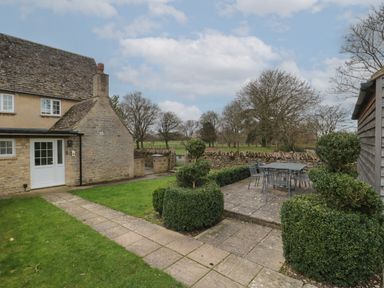 A garden patio with outdoor dining table and chairs next to a stone cottage at Stable Cottage in Lechlade-On-Thames