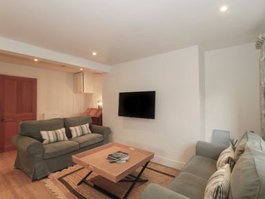A living room with two sofas a wooden coffee table a wall-mounted TV and a wooden door at Stable Cottage in Lechlade-On-Thames