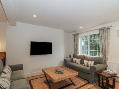 A living room with two sofas a wooden coffee table a wall-mounted tv and a window at Stable Cottage in Lechlade-On-Thames
