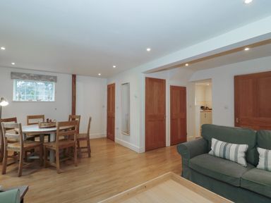 A dining area with wooden chairs around a round table and a green sofa in a living room at Stable Cottage in Lechlade-On-Thames