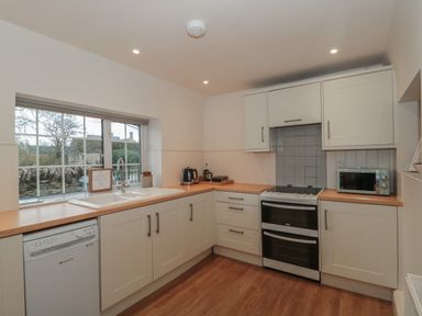 A kitchen with white cabinets a dishwasher stove microwave and sink under a window at Stable Cottage in Lechlade-On-Thames