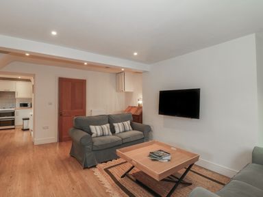 A living room with grey sofas a wooden coffee table a wall-mounted tv and wooden flooring at Stable Cottage in Lechlade-On-Thames