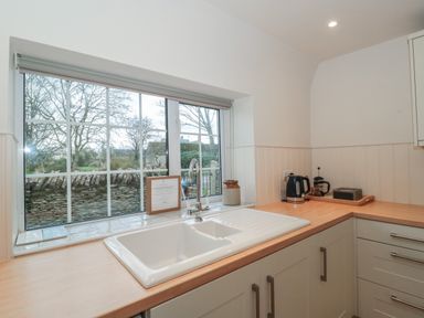 A kitchen sink under a window with a kettle and coffee maker on the countertop at Stable Cottage in Lechlade-On-Thames