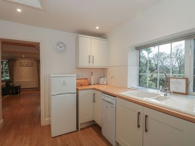 A kitchen with a white refrigerator a dishwasher a sink under a window and wooden countertops at Stable Cottage in Lechlade-On-Thames