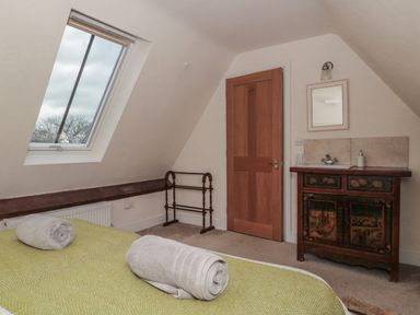 A bedroom with a bed covered in green bedding and rolled towels a wooden door a decorative cabinet with a sink and a mirror at Stable Cottage in Lechlade-On-Thames
