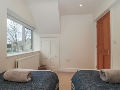 A bedroom with two single beds with towels on them a window a small door and a wooden door at Stable Cottage in Lechlade-On-Thames