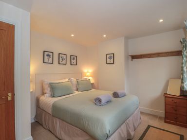 A bedroom with a double bed two rolled towels wooden chest of drawers and framed pictures on the wall at Stable Cottage in Lechlade-On-Thames