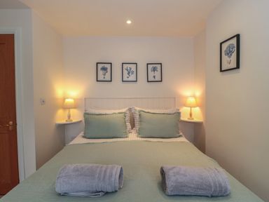 A bedroom with a double bed two lamps and framed pictures on the walls at Stable Cottage in Lechlade-On-Thames