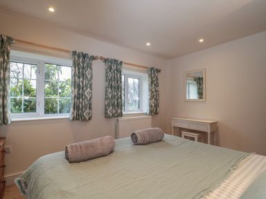 A bedroom with a bed with towels on it two windows with patterned curtains a dressing table with a mirror at Stable Cottage in Lechlade-On-Thames