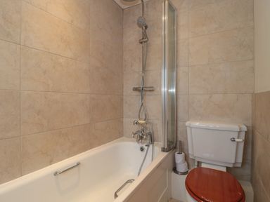 A bathroom with a bathtub and a showerhead next to a toilet with a wooden seat at Stable Cottage in Lechlade-On-Thames
