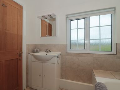 A bathroom with a sink cabinet a mirror wooden door and a window at Stable Cottage in Lechlade-On-Thames