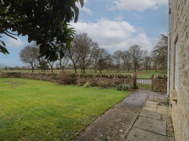 A garden with a stone wall and metal gate next to a stone house at Stable Cottage in Lechlade-On-Thames