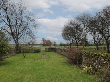 A garden with grass trees and a stone wall next to a country road at Stable Cottage in Lechlade-On-Thames