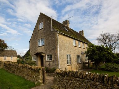 A stone house with multiple windows and a stone wall in front at Stable Cottage in Lechlade-On-Thames
