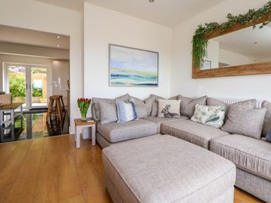A living room with a large gray sectional sofa wooden floor a side table with red flowers and a painting on the wall at Buzzards View in Dyserth