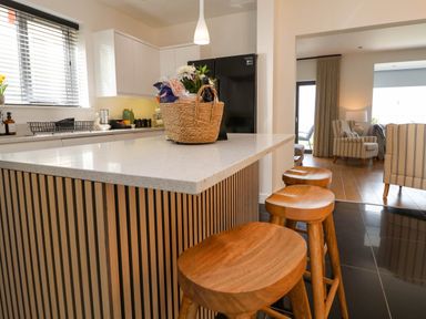 A kitchen with wooden stools at a breakfast bar and a basket on the counter at Buzzards View in Dyserth
