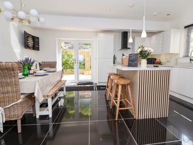 A kitchen with a dining table set with dishes and chairs next to a kitchen island with stools and pendant lights at Buzzards View in Dyserth