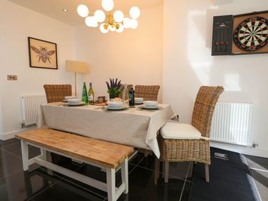 A dining area with a table set for four people with woven chairs a bench a dartboard on the wall and a framed picture of a bee on the wall at Buzzards View in Dyserth